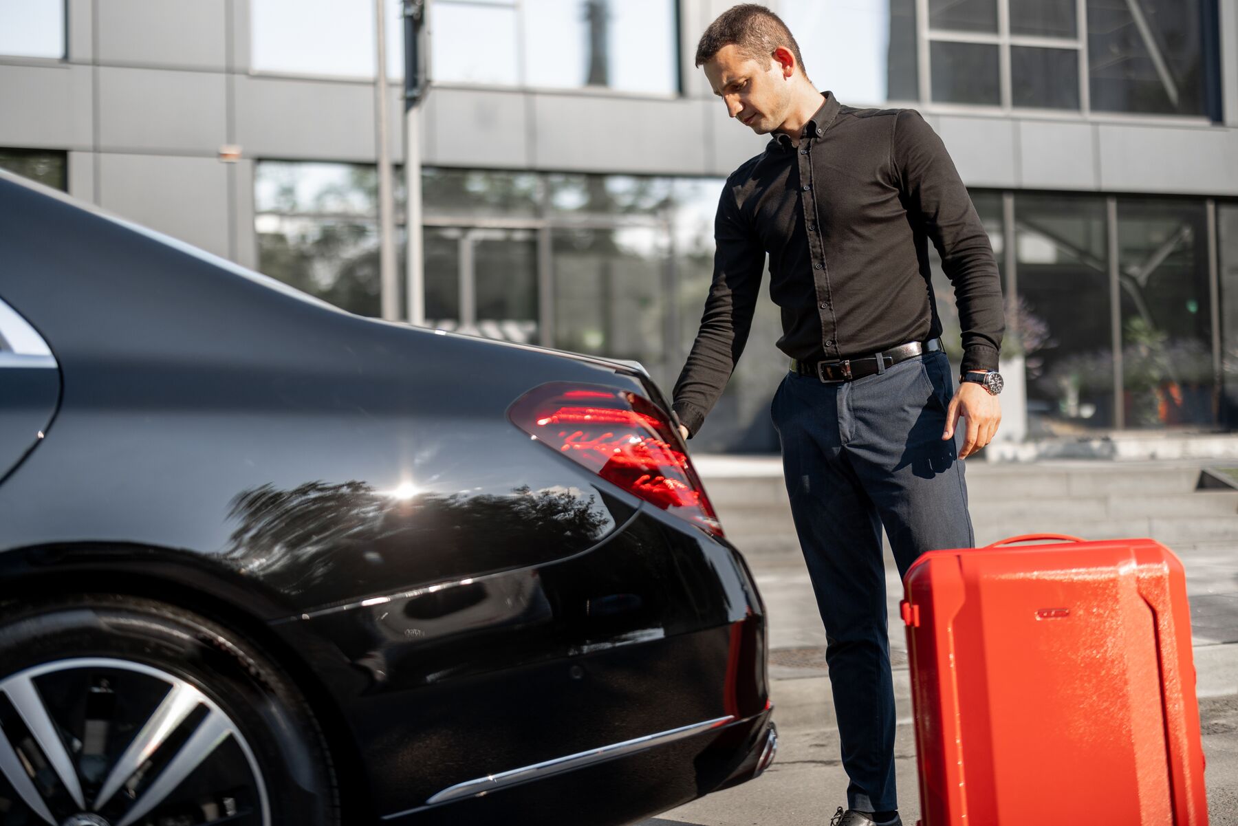 Chauffeur loading luggage curbside before a shuttle transfer.